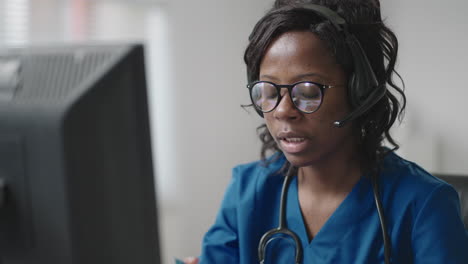 Black-Woman-doctor-wear-white-coat-glasses-and-headset-talking-to-client-use-videocall.-Due-coronavirus-pandemic-outbreak-therapist-working-remotely-provide-help-to-clinic-patients-by-video-call